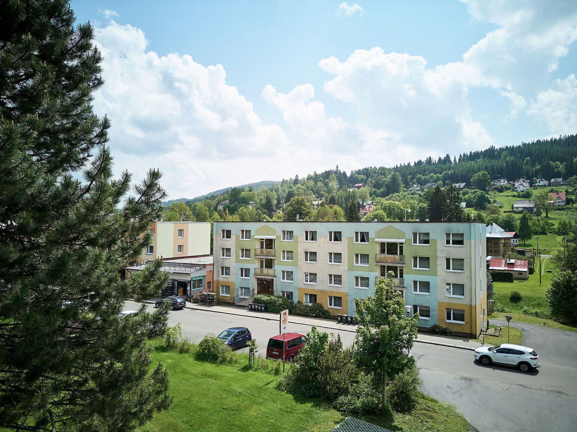 A multi-story building with a parking lot in front, surrounded by greenery and hills.