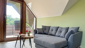A modern living room with a grey sectional sofa, a small round table with a vase of flowers, and a sliding glass door leading to an outdoor area.