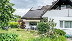 A modern house with a sloped roof, solar panels, and a garden with various plants and flowers.