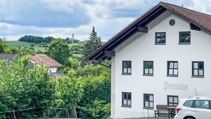 Ein weißes Gebäude mit dem Schriftzug 'Pension' auf der Fassade, umgeben von Grünpflanzen und blauem Himmel.