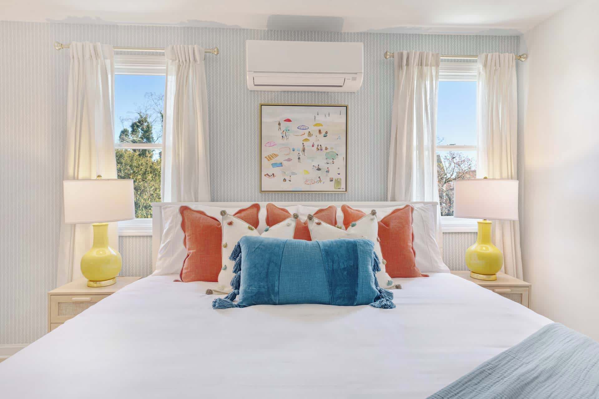 Une chambre à coucher avec un grand lit, deux lampes de chevet, un appareil de climatisation et une fenêtre avec des rideaux.