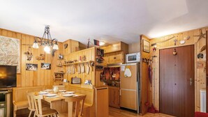 A compact kitchen with wooden cabinets, a dining table with chairs, a refrigerator, and a microwave. - Nice apartment for 3 people with terrace (Canazei)