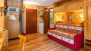 A compact living space with a kitchenette, a red sofa, wooden flooring, and a small dining area. - Nice apartment for 3 people with terrace (Canazei)
