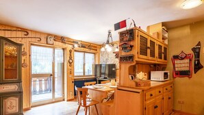 A wooden interior with a dining area, kitchen, and a large window. - Nice apartment for 3 people with terrace (Canazei)