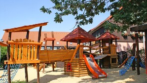 Une aire de jeux avec un toboggan en bois, des structures d’escalade et un filet en corde.
