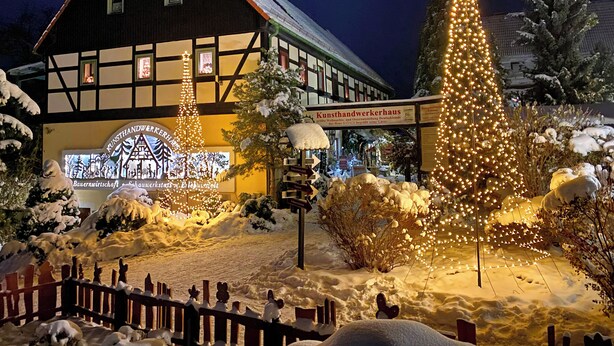 Un bâtiment traditionnel à colombages, avec une enseigne indiquant « Kunsthandwerkerhaus », et un grand sapin de Noël illuminé.