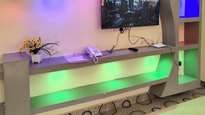 Een receptiebalie met een televisiescherm waarop een stadsgezicht te zien is, een telefoon en een bloemenvaas.
