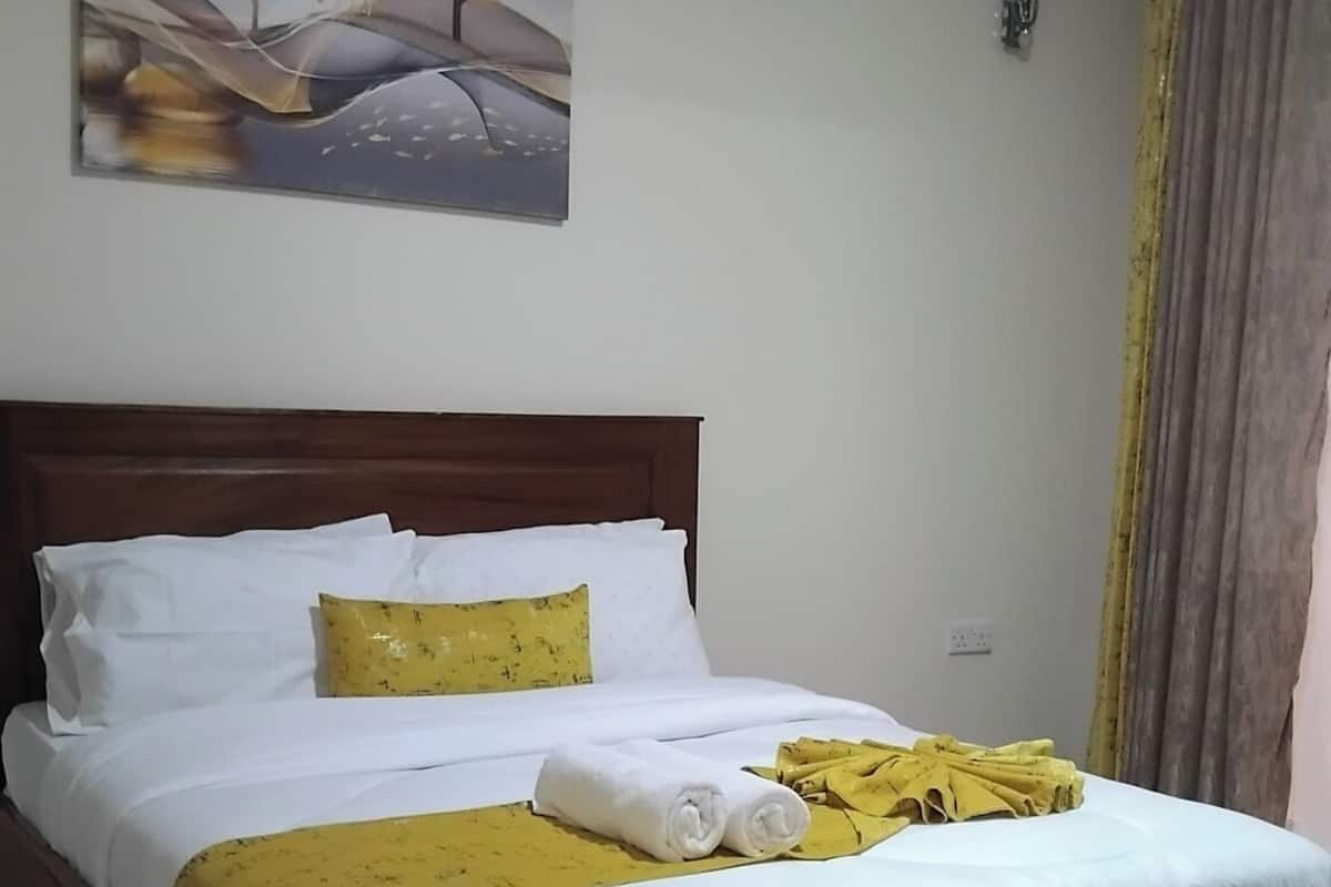 Una cama bien hecha con ropa de cama blanca y amarilla, un cabecero de madera y un cuadro sobre ella.