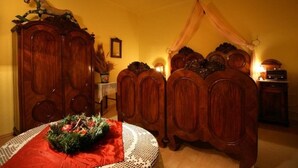 Una habitación tradicional con un armario de madera, una mesa con mantel rojo y una cama con dosel.