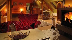 Una sala de estar acogedora con un sillón rojo, una mesa de centro de vidrio con una bandeja decorativa, una chimenea y una zona de comedor con una mesa y sillas.