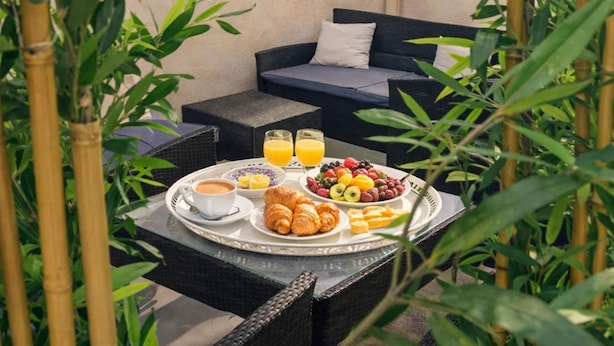 A breakfast setup with croissants, fruit, and juice on a tray, a sofa, and bamboo plants in a courtyard. - 1607 Brancion (Paris)