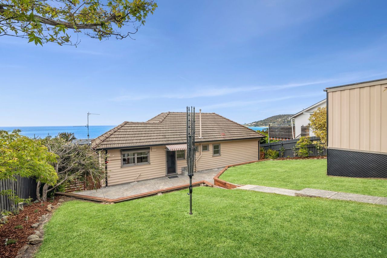A residential property with a well-maintained lawn, a house with a tiled roof, and a clear view of the sea in the background.