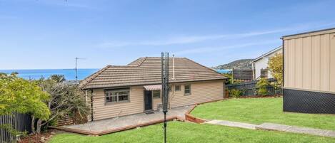 A residential property with a well-maintained lawn, a house with a tiled roof, and a clear view of the sea in the background.