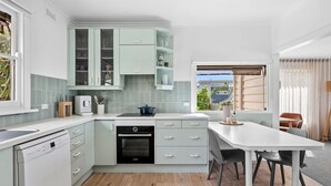 A modern kitchen with light green cabinets, a built-in oven, and a dining area with a white table and chairs.
