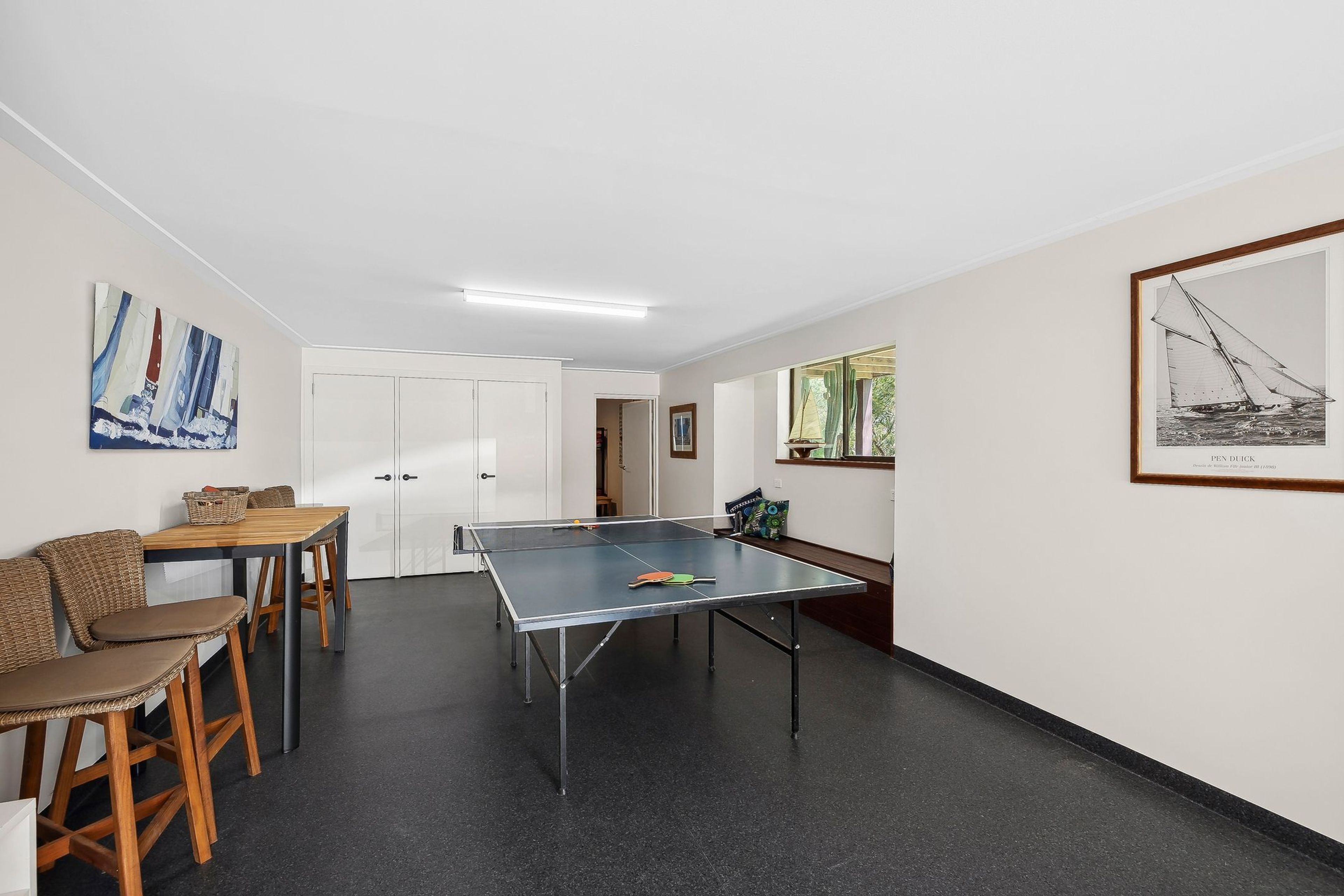 A room with a ping pong table, a seating area with chairs, and a door leading to another room.
