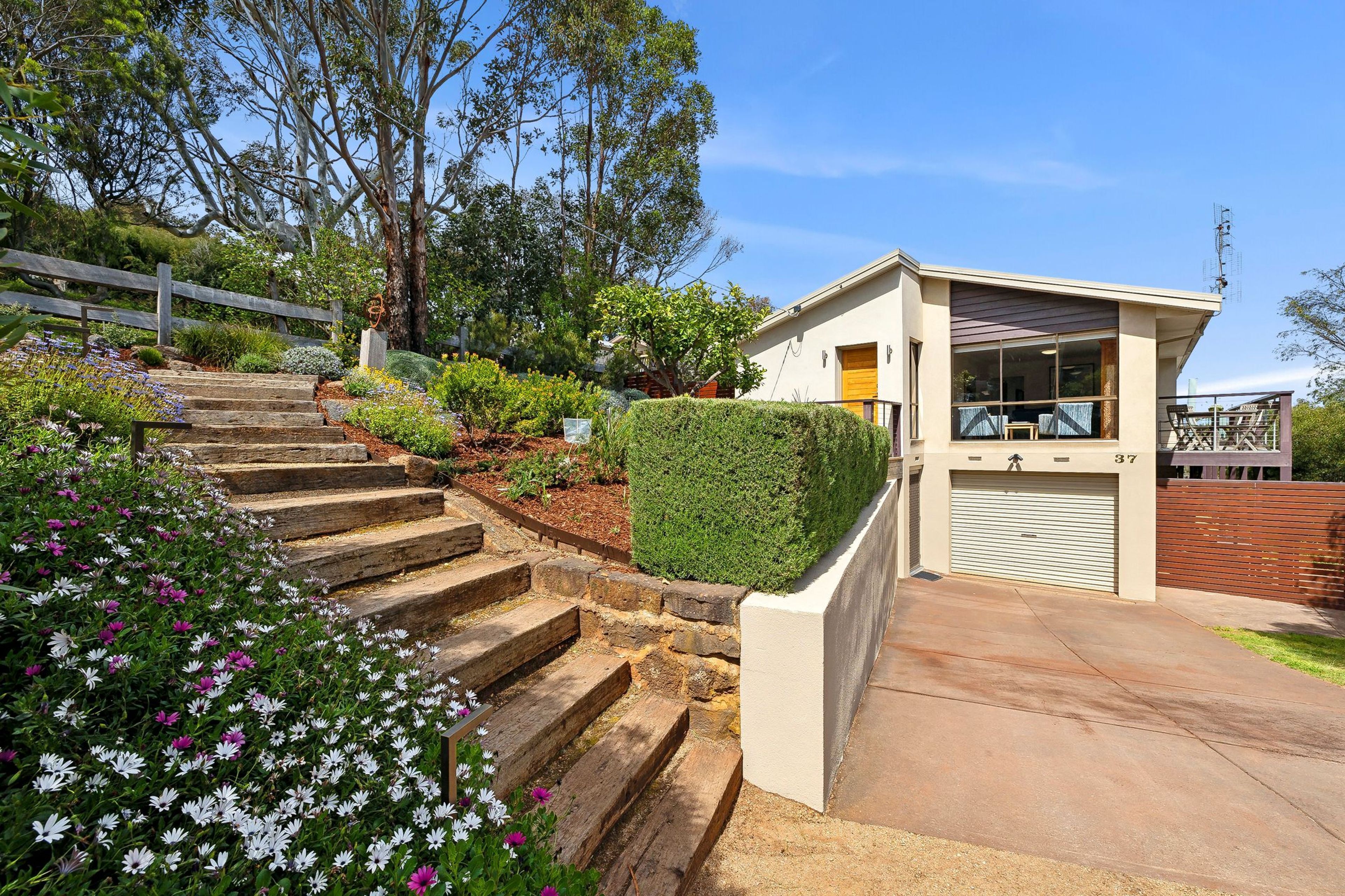 A residential property with a staircase leading to a garage, surrounded by a garden with various plants and flowers.