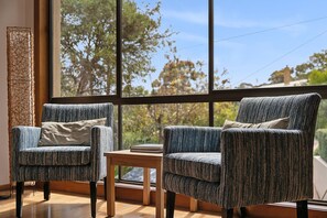 A room with two armchairs, a small table, and a large window with a view of trees.