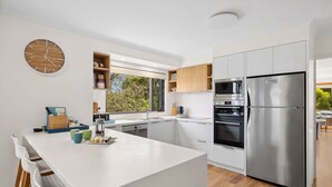A modern kitchen with a central island, built-in appliances, and a large window. - BeachHaven (Aireys Inlet)