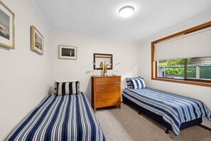 A bedroom with two single beds, a dresser, and a window with a view of greenery. - BeachHaven (Aireys Inlet)