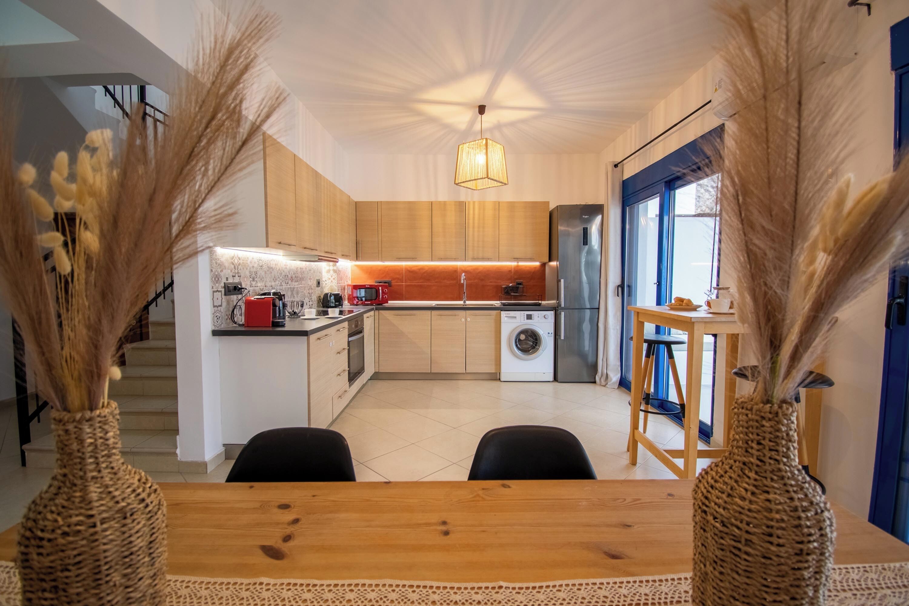 Eine moderne Küche mit Holzschränken, einem Edelstahl-Kühlschrank, einer Waschmaschine und einer Essecke mit Holztisch und Stühlen.