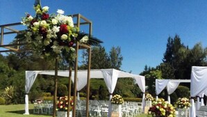 An outdoor wedding setup with a white aisle, floral decorations, and a clear blue sky.