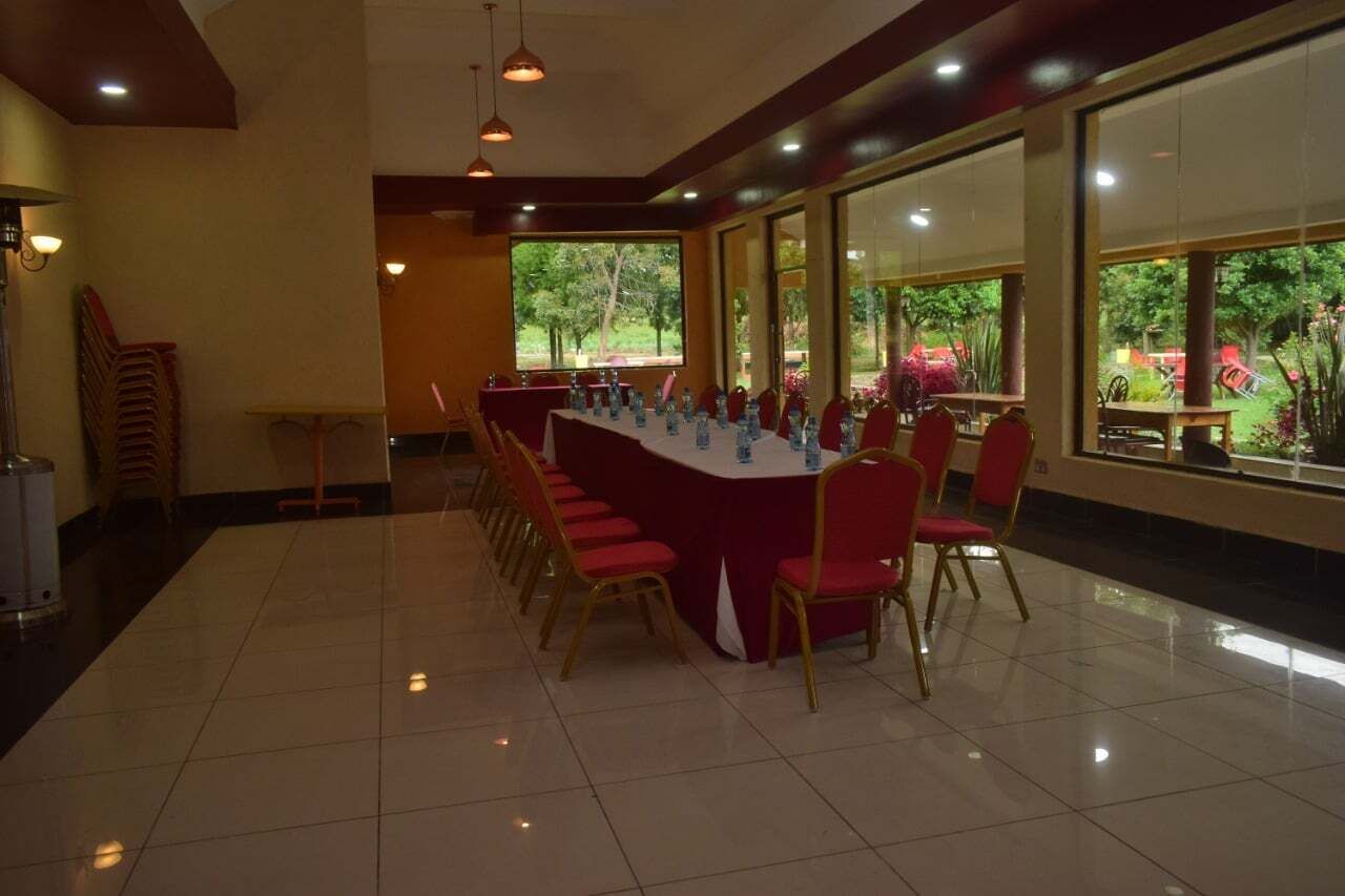 A conference room with a long table, red chairs, and a view of greenery through large windows.