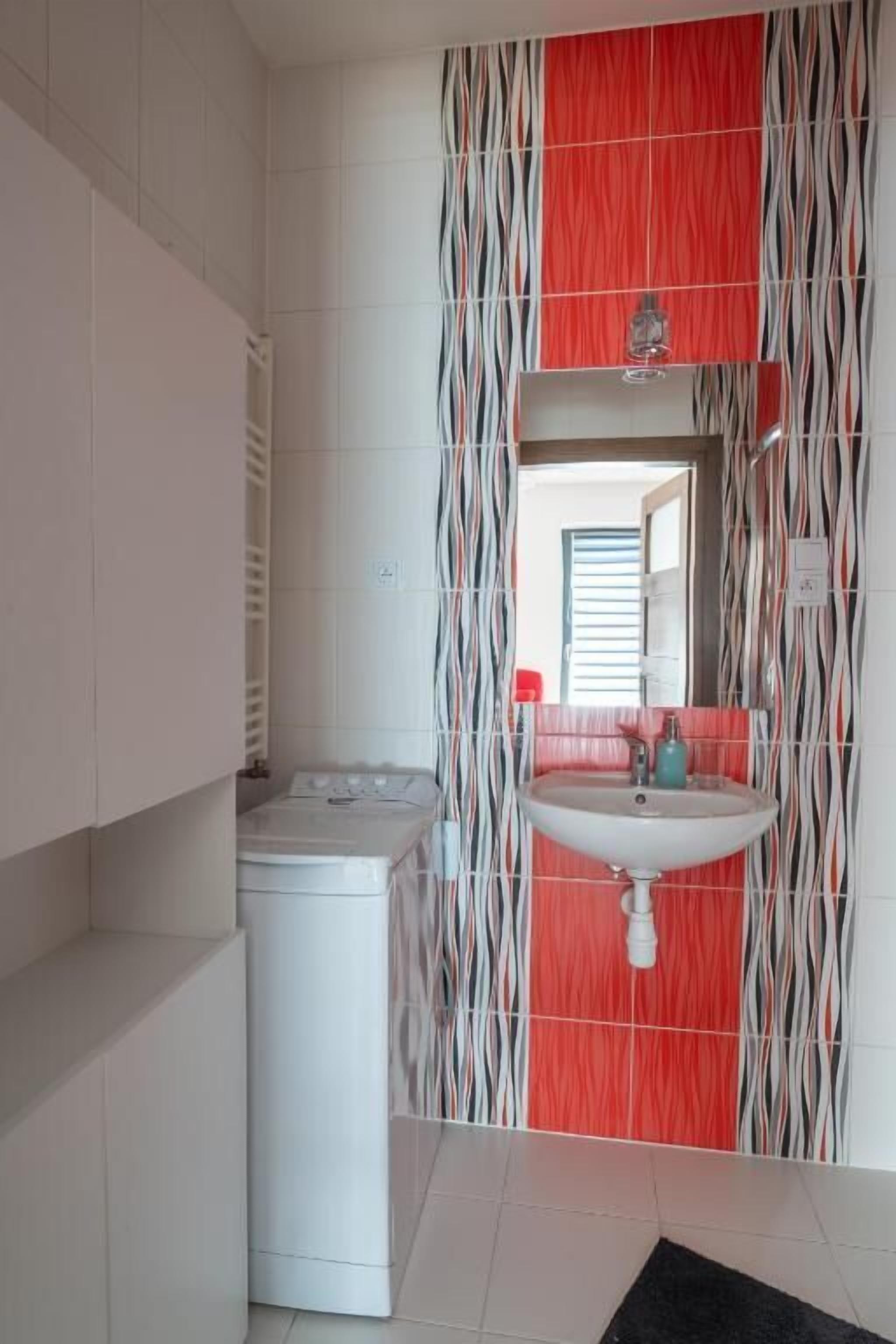Un baño con lavadora blanca, lavamanos y espejo.