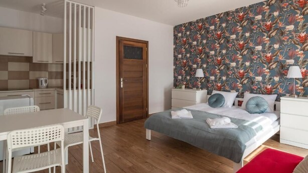 A compact bedroom with a bed, bedside tables, a wardrobe, and a small kitchenette. - Przytulny apartament KOLEJOVA 12 (Nowy Targ)