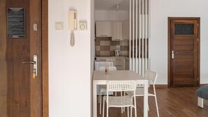 A modern kitchen with white cabinets, a wooden door, and a dining area with a white table and chairs. - Przytulny apartament KOLEJOVA 12 (Nowy Targ)