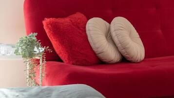 Un divano rosso con due cuscini beige, una piccola pianta e una TV nera montata su una parete color pesca.