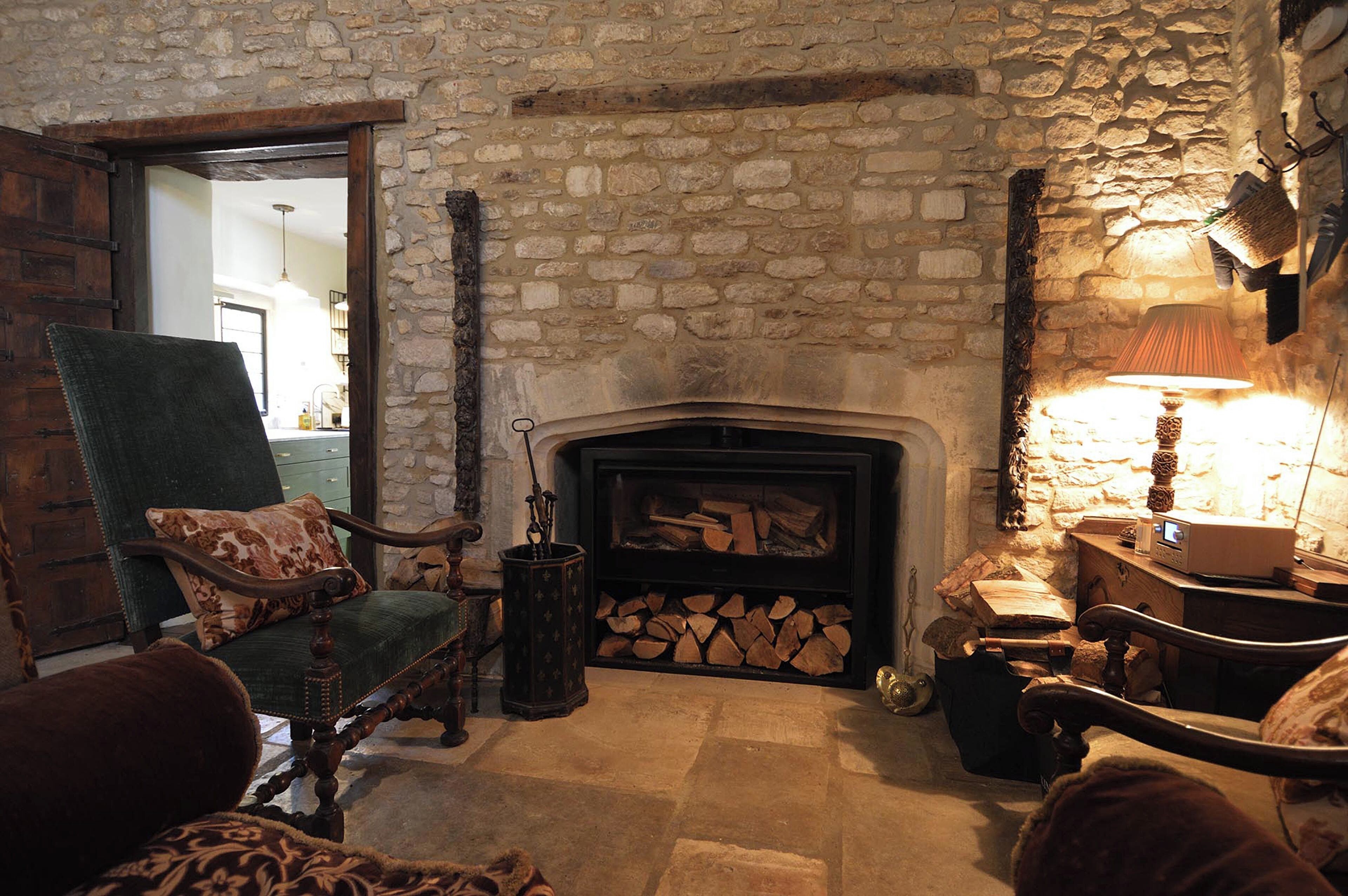 A cozy room with a stone fireplace, a green armchair, and a wooden cabinet.