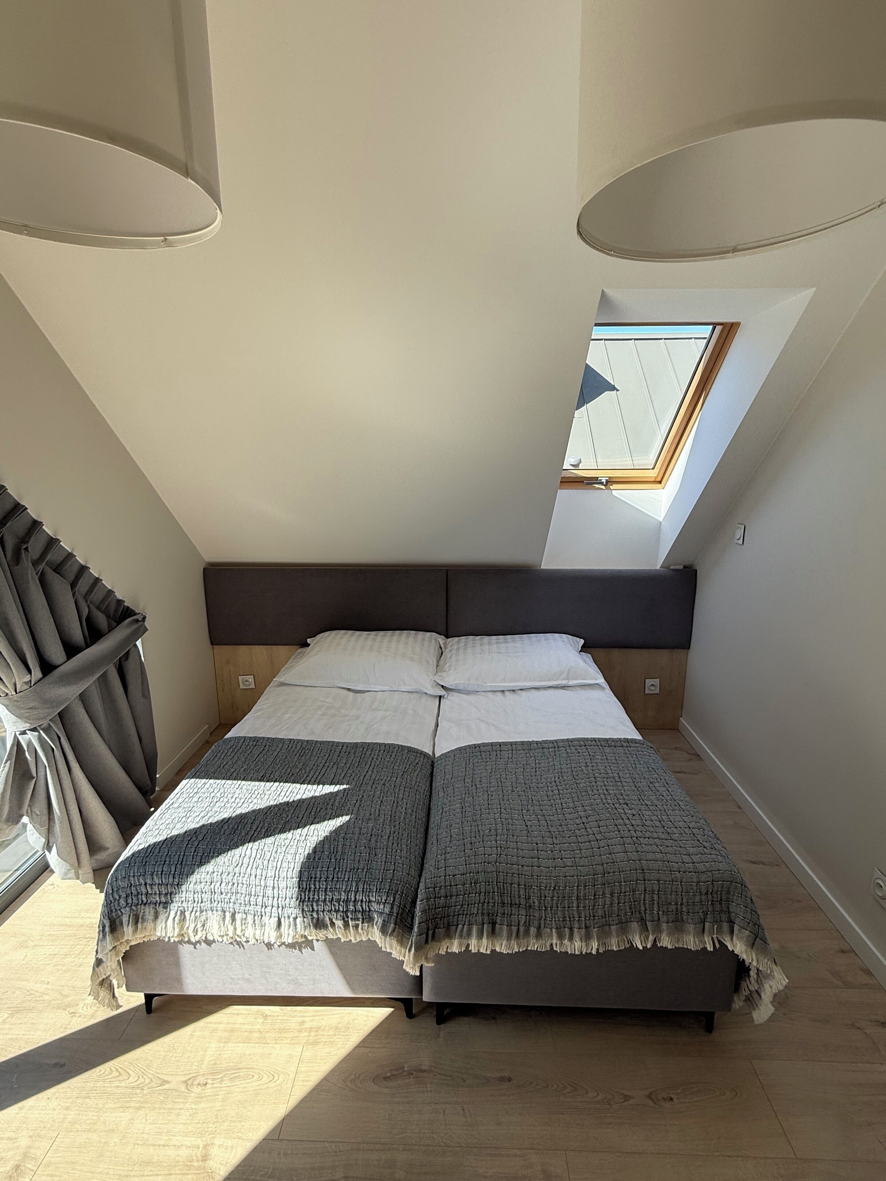 Una camera da letto con una finestra a lucernario, un letto con coperta grigia e una finestra con tende.