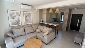 A modern living room with a grey sectional sofa, a round wooden coffee table, and two wall-mounted air conditioners. - Charming 2-bedroom bungalow with AC, WiFi in enchanting Niesulice for 6 person (Niesulice)