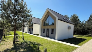 A modern building with a triangular roof and large windows, surrounded by a well-maintained lawn and trees. - Charming 2-bedroom bungalow with AC, WiFi in enchanting Niesulice for 6 person (Niesulice)