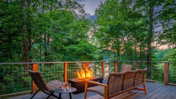 Um deck com lareira, móveis de vime e vista para uma área arborizada.