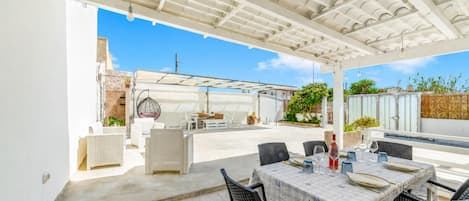 An outdoor patio with a table set for dining, surrounded by chairs, and a pool area in the background.