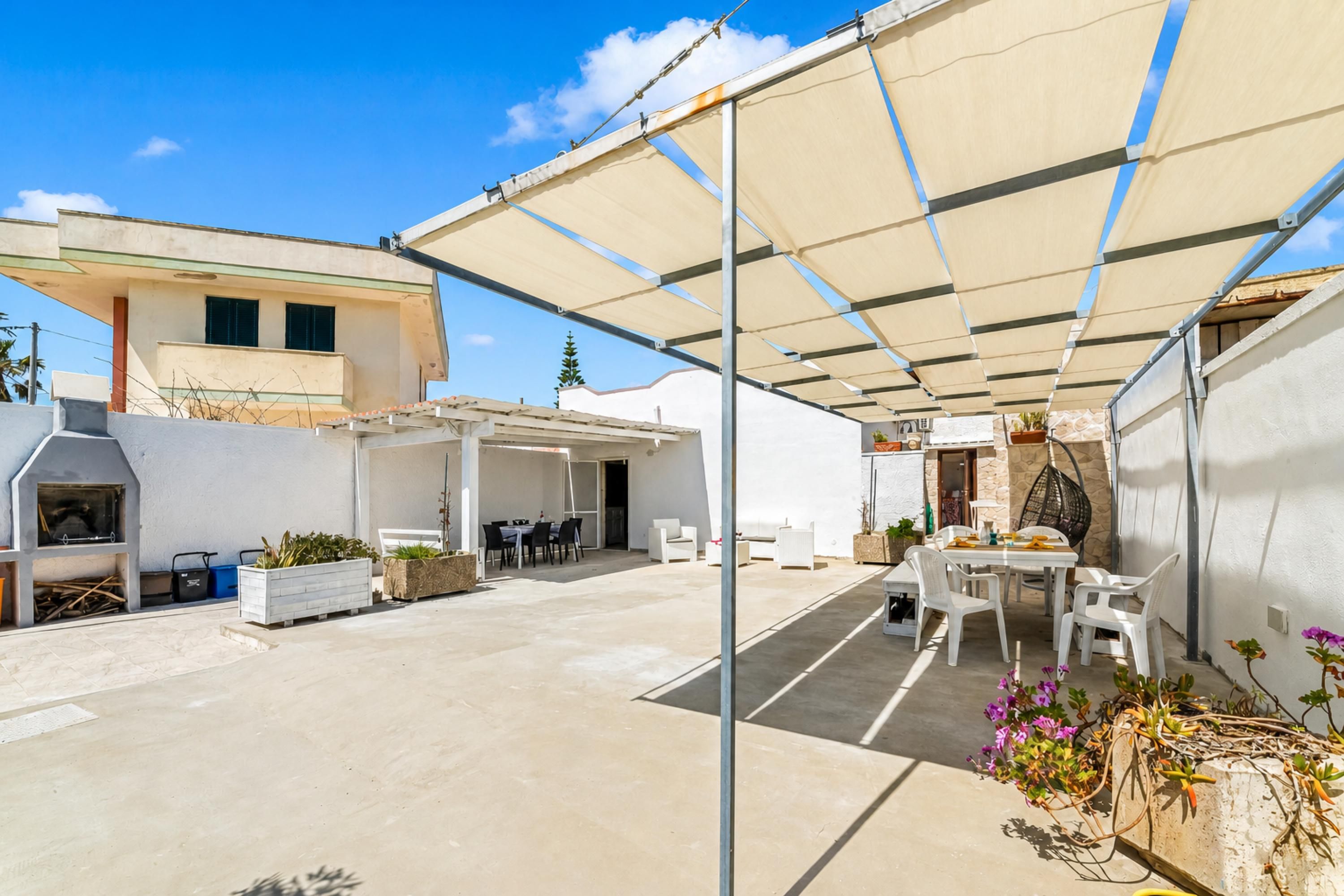 Eine überdachte Terrasse mit Barbereich, Esstisch und Stühlen.