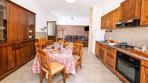 A kitchen with wooden cabinets, a dining table set for four, and a brick wall in the background. - Villa Benedetta 50m From Beach (Lecce)
