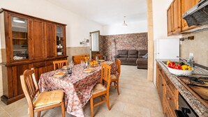 A dining area with a table set for four, wooden chairs, a cabinet with glass doors, and a brick wall in the background. - Villa Benedetta 50m From Beach (Lecce)
