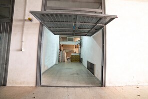 Un couloir étroit avec une porte en métal qui donne sur une pièce où se trouvent un vélo et un lit.