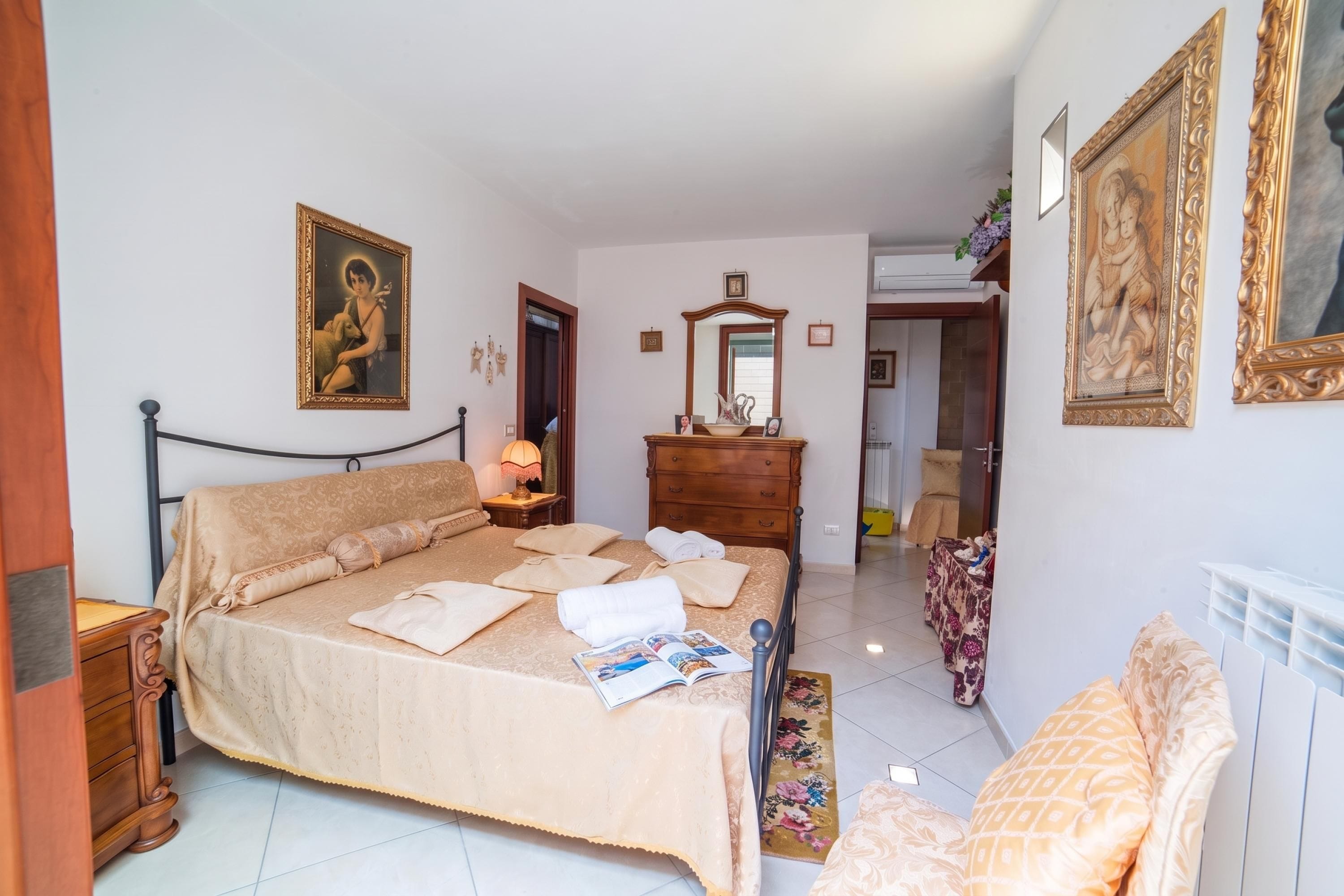 A bedroom with a bed, bedside tables, a dresser, a mirror, and framed artwork on the walls.
