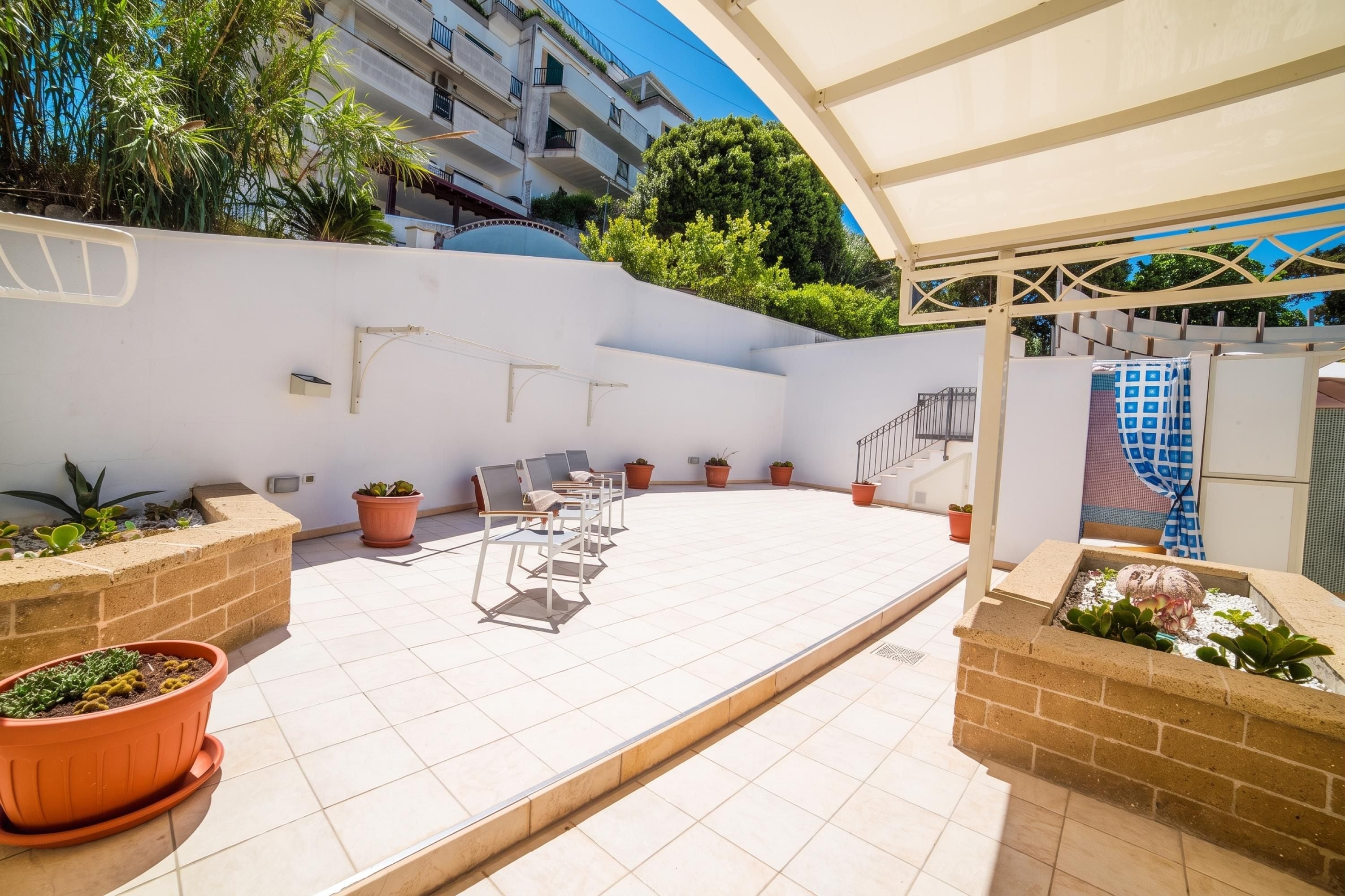 A covered outdoor patio with tiled flooring, potted plants, and outdoor furniture.