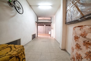 Un pasillo estrecho con una bicicleta colgada en la pared, una puerta al final y un colchón con estampado floral a la derecha.