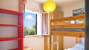 A room with a bunk bed, a desk, a chair, a window with a view of greenery, and a door with a patterned curtain. - Eurovillage Apartment With Pool & Terrace (Porto Cesareo)