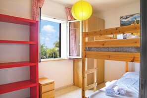 Una habitación con literas, un escritorio, una silla, un ventanal con vistas a la vegetación y una puerta con cortina estampada.
