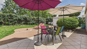 A patio area with outdoor furniture, including a table and chairs, and two umbrellas providing shade.