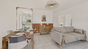 A modern living room with a sofa, a dining table with chairs, and a kitchen area in the background.