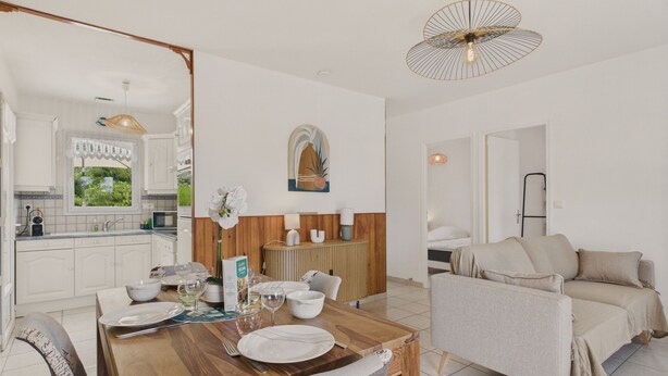 A modern living room with a dining area, a sofa, and a kitchen visible through an open door.