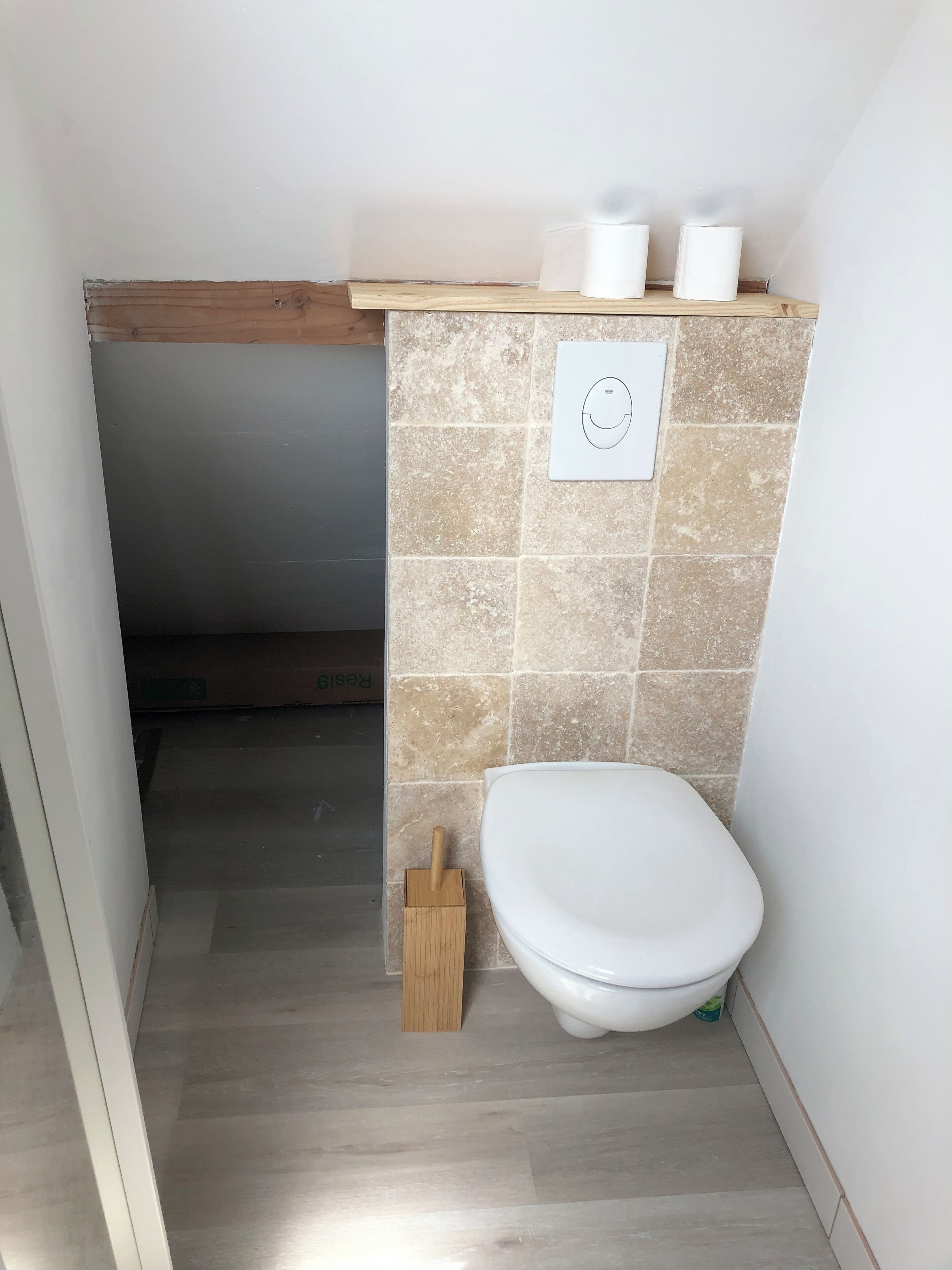 A small bathroom with a toilet, a wooden floor, and beige tiles on the wall.