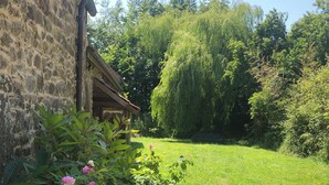 Ein Steinhaus mit einer Holzveranda, umgeben von üppigem Grün und blühenden Pflanzen.